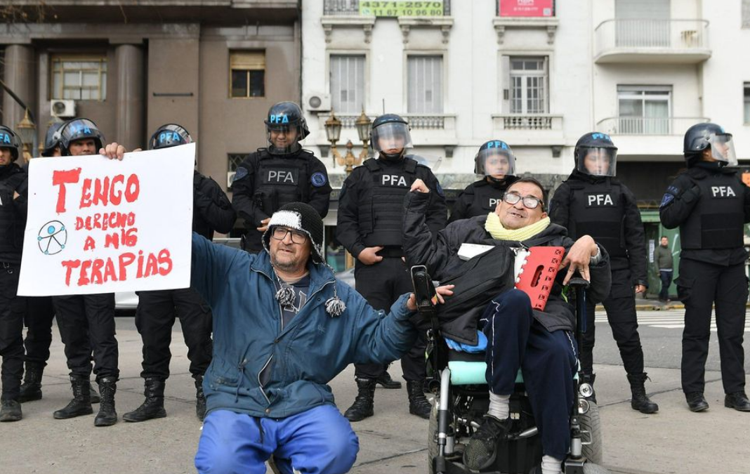Foto de persona en silla de ruedas y su cuidador manifestándose en Argentina