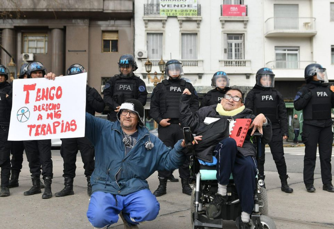Foto de persona en silla de ruedas y su cuidador manifestándose en Argentina