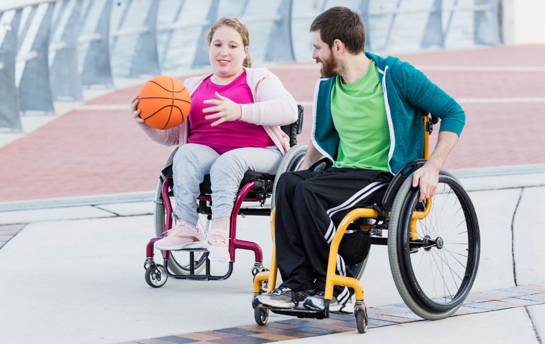 Mujer en silla de ruedas con una pelota de básquetbol en su mano y junto a ella un hombre en silla de ruedas
