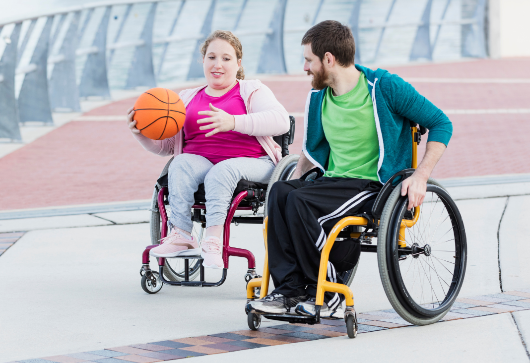 Mujer en silla de ruedas con una pelota de básquetbol en su mano y junto a ella un hombre en silla de ruedas