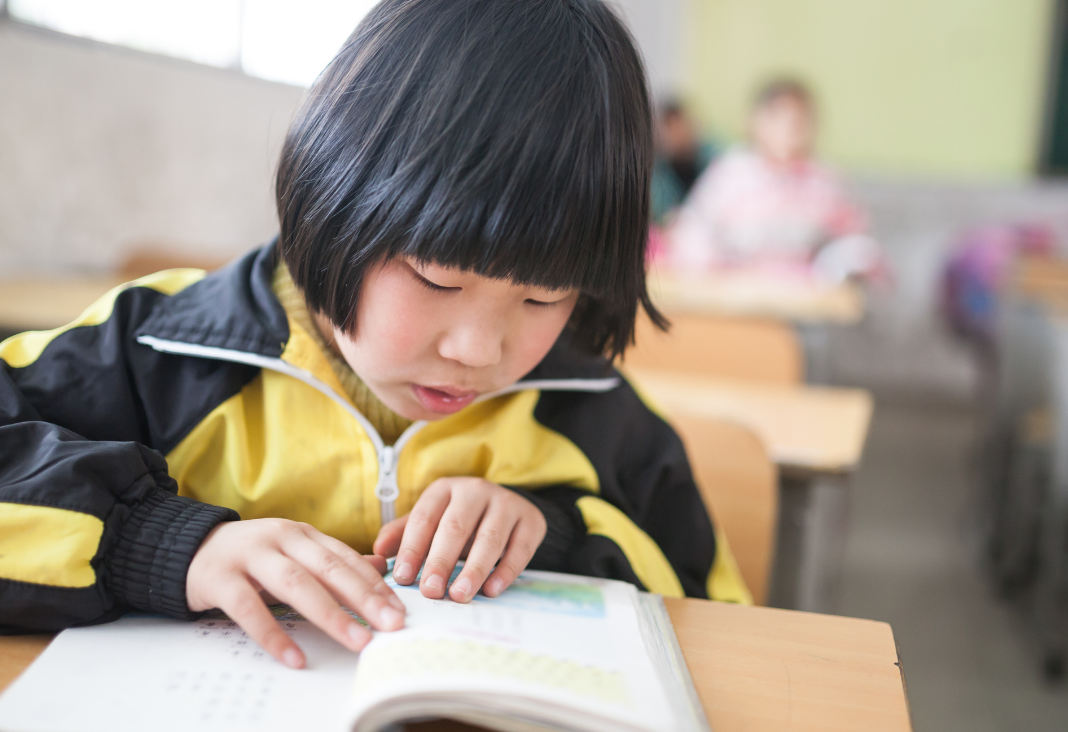 Niña china leyendo sentada en una sala de clases