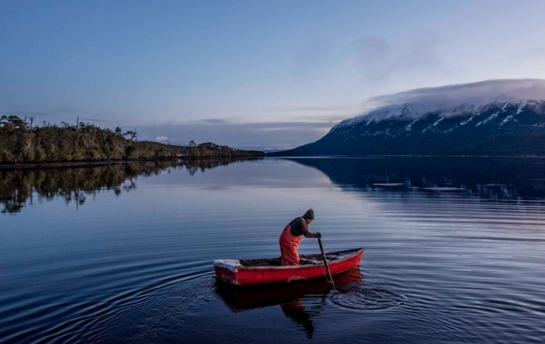 Foto de un pescador artesanal en un bote en medio de un lago en el sur de Chile