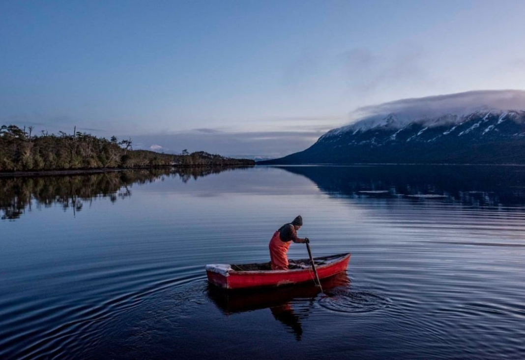 Foto de un pescador artesanal en un bote en medio de un lago en el sur de Chile