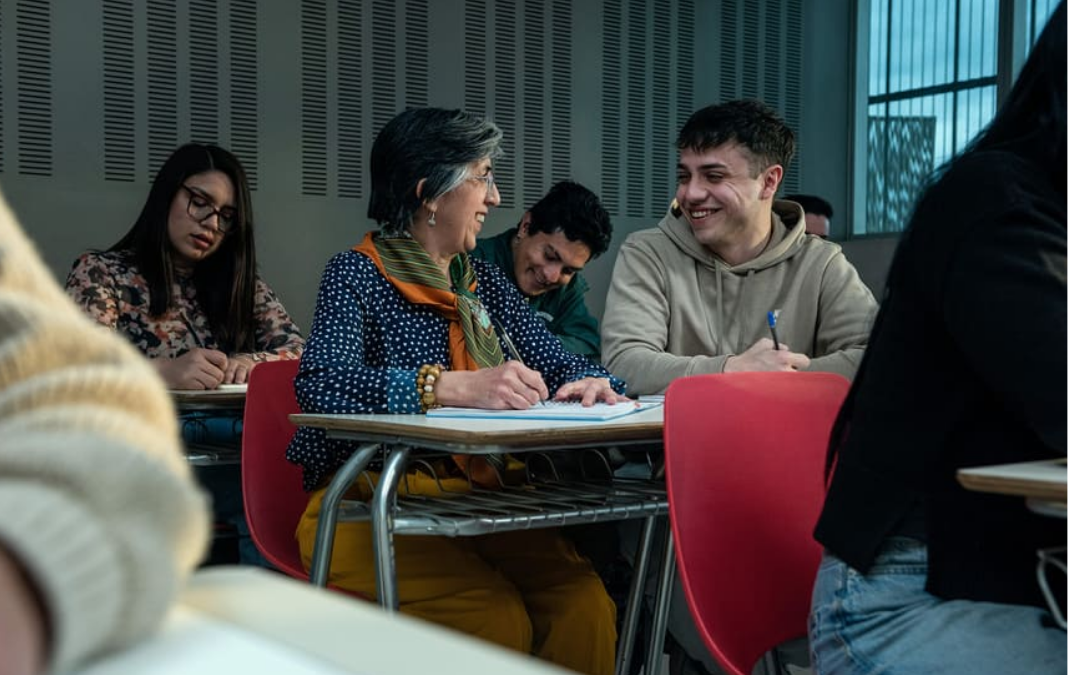 Fotografía de una sala de clases universitaria y una mujer mayor hablando con un joven