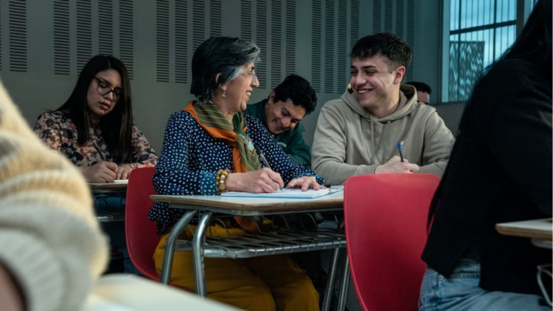 Fotografía de una sala de clases universitaria y una mujer mayor hablando con un joven