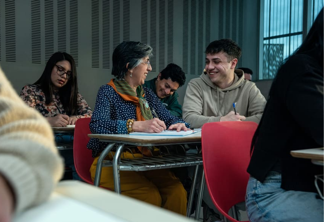 Fotografía de una sala de clases universitaria y una mujer mayor hablando con un joven