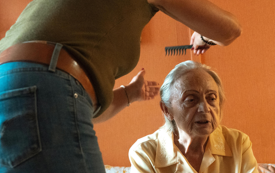 Mujer de pie peinando a una adulta mayor sentada