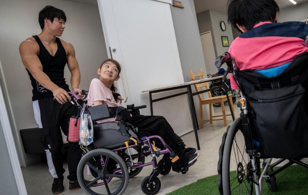 Foto de una residencia y un culturista ayudando a una mujer en silla de ruedas