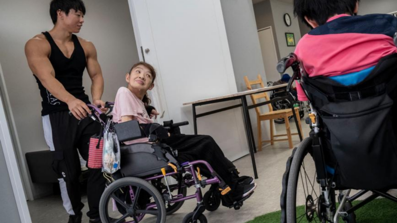 Foto de una residencia y un culturista ayudando a una mujer en silla de ruedas