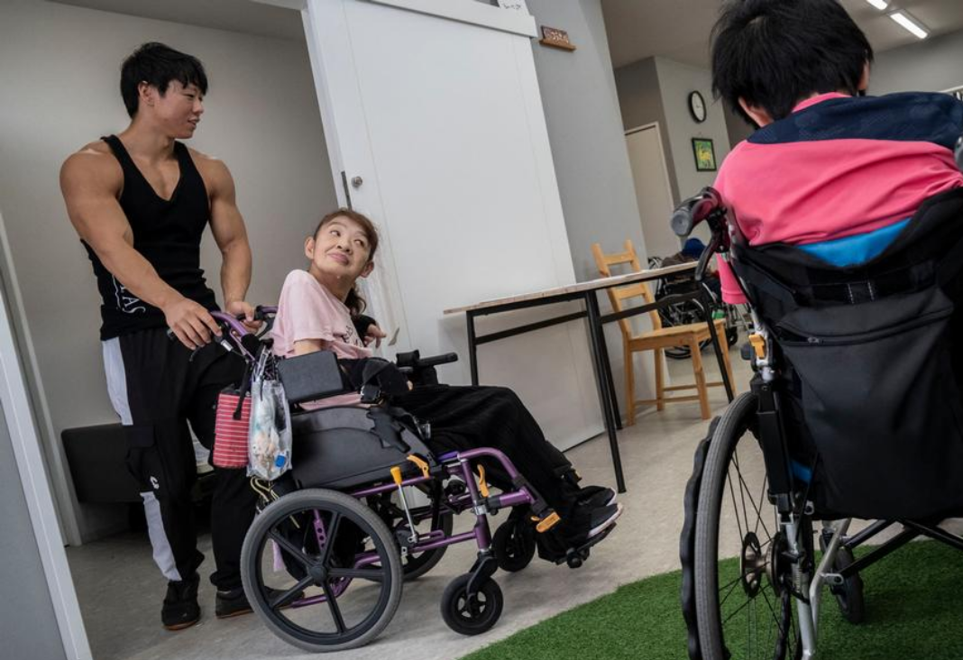 Foto de una residencia y un culturista ayudando a una mujer en silla de ruedas