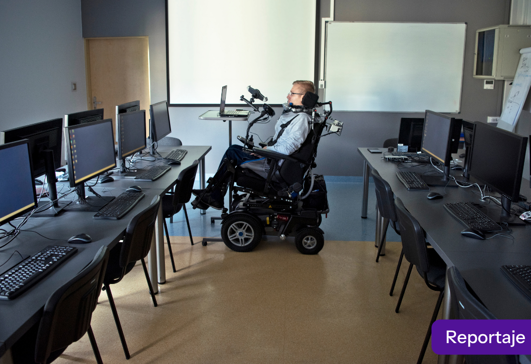 Foto de una persona en silla de ruedas en una sala de universidad llena de compitadores