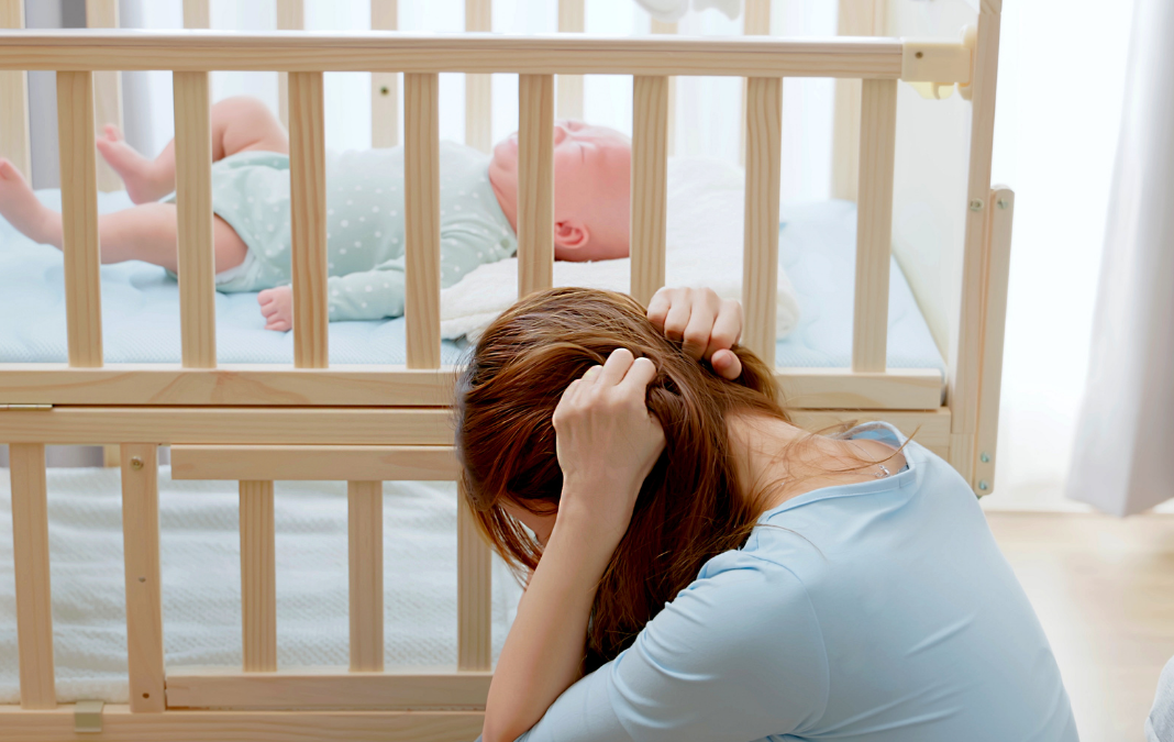 Mujer tapándose los oídos junto a una cuna y dentro de ella un bebé llorando