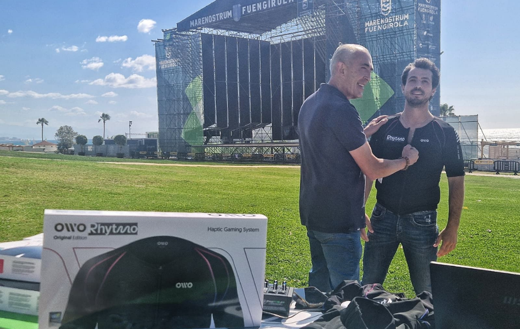 Dos hombres probando una polera háptica y detrás el escenario para un concierto