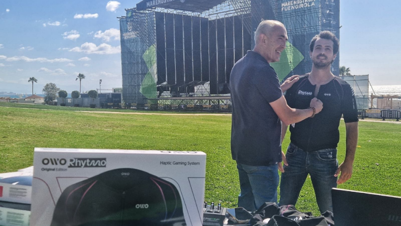 Dos hombres probando una polera háptica y detrás el escenario para un concierto