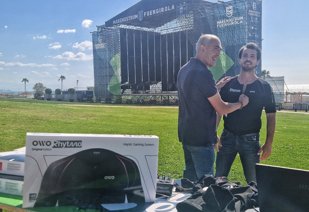 Dos hombres probando una polera háptica y detrás el escenario para un concierto