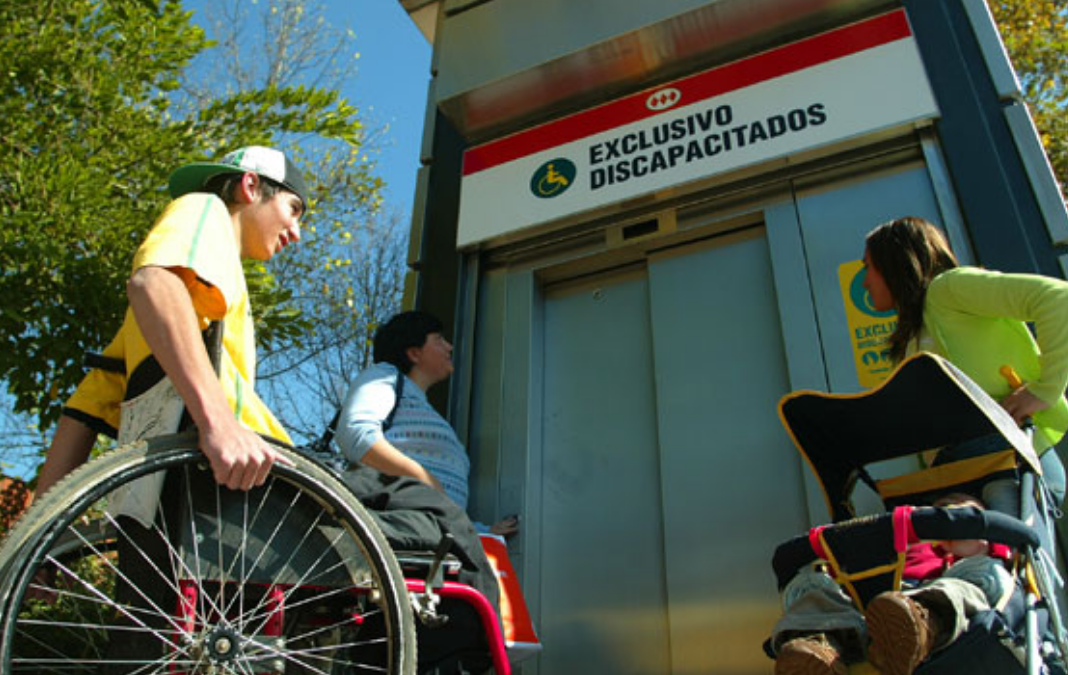 Tres personas esperando ascensor de metro: una señora, un hombre en silla de ruedas y una mujer con un coche