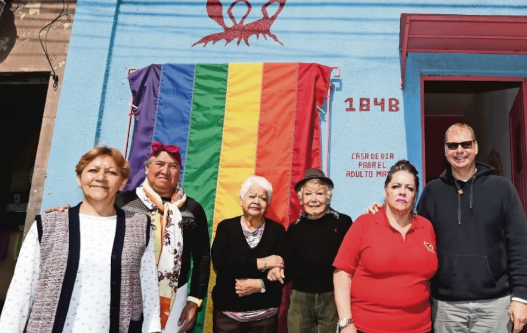 Cinco personas mayores y atrás una bandera LGTBQIA+