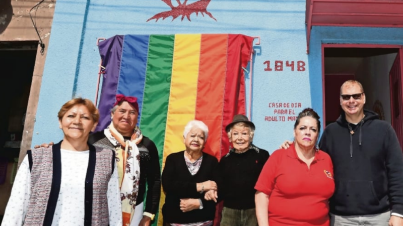 Cinco personas mayores y atrás una bandera LGTBQIA+