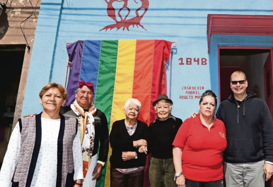 Cinco personas mayores y atrás una bandera LGTBQIA+