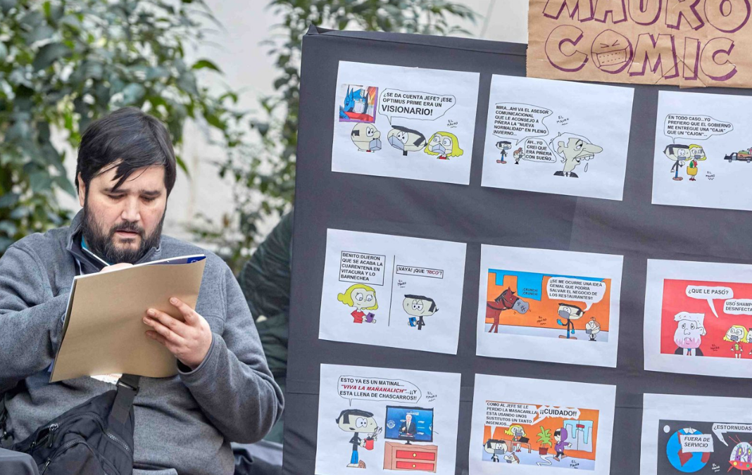 Hombre sentado dibujando junto a un mural llenos de comics