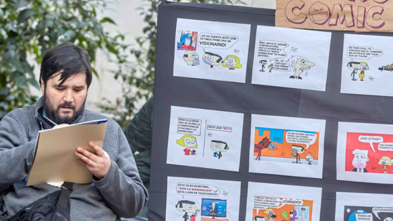 Hombre sentado dibujando junto a un mural llenos de comics
