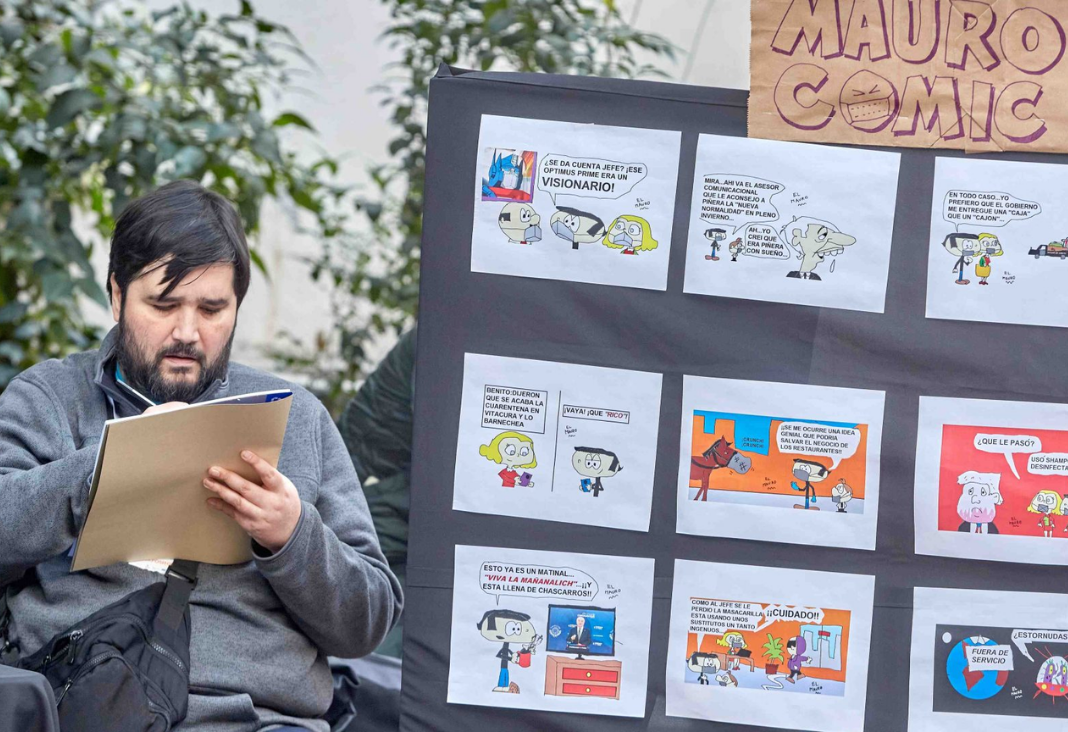 Hombre sentado dibujando junto a un mural llenos de comics