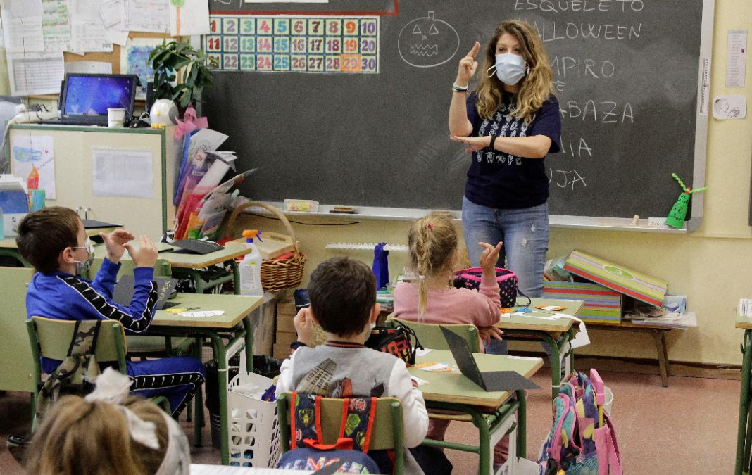 Mujer enseñando lengua de señas a niñas y niños en una sala de clases