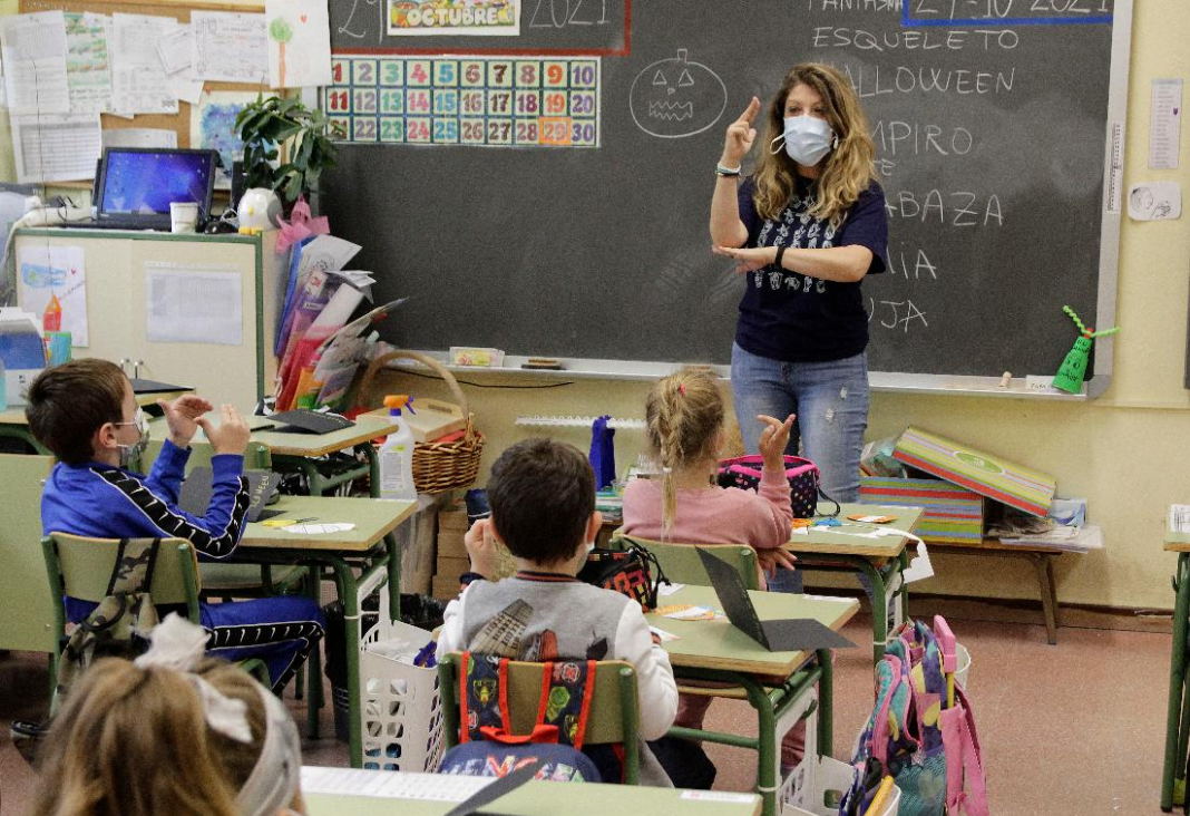 Mujer enseñando lengua de señas a niñas y niños en una sala de clases