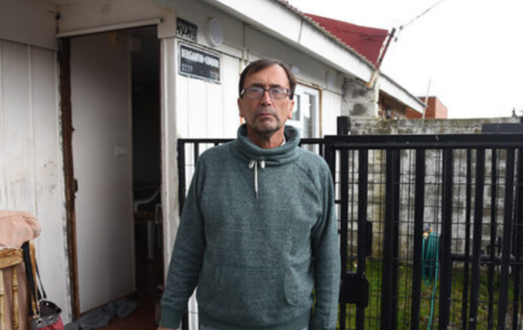 Hombre con anteojos y polerón gris afuera de su casa