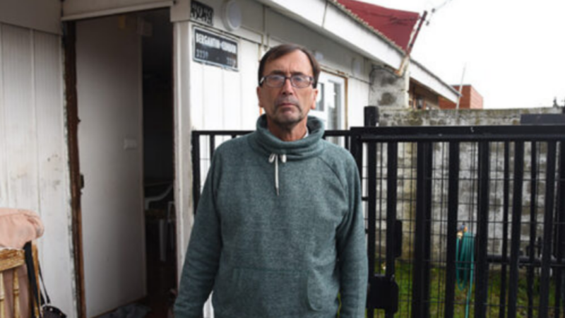 Hombre con anteojos y polerón gris afuera de su casa