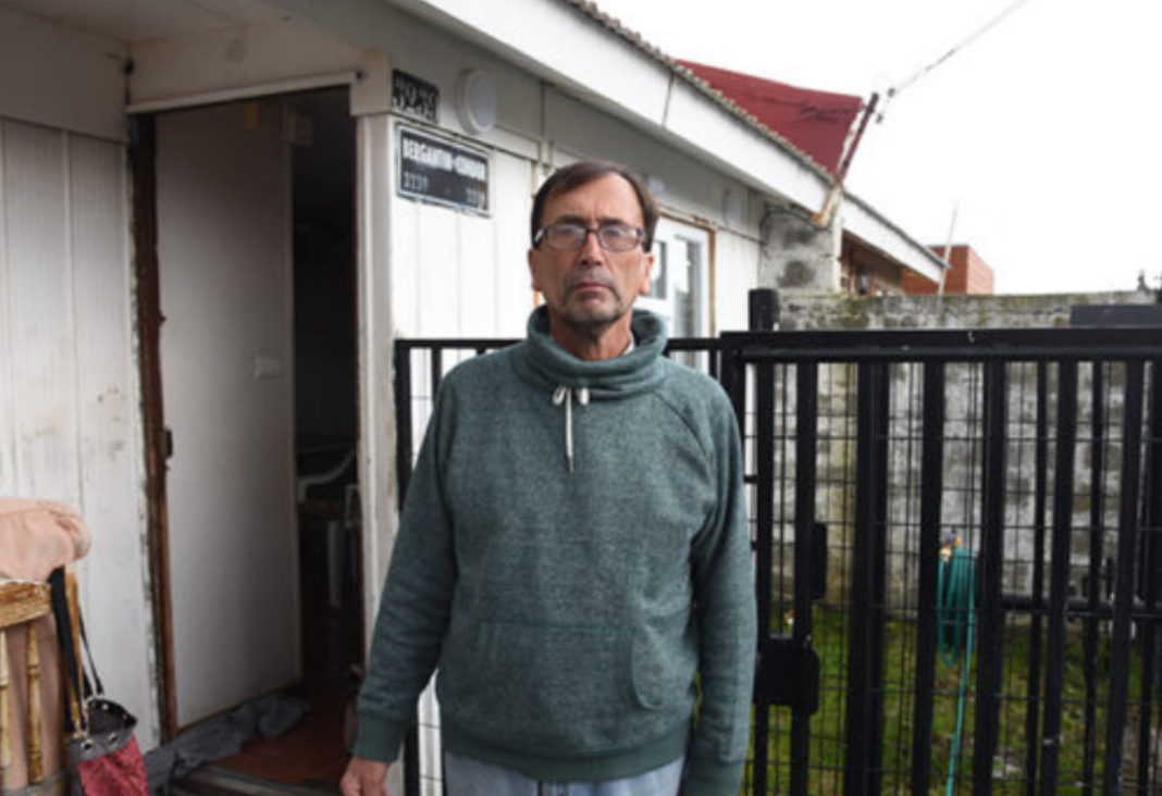 Hombre con anteojos y polerón gris afuera de su casa