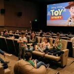 Diversas personas adultas e infantes en una sala de cine y en la pantalla imagen de la película Toy Story