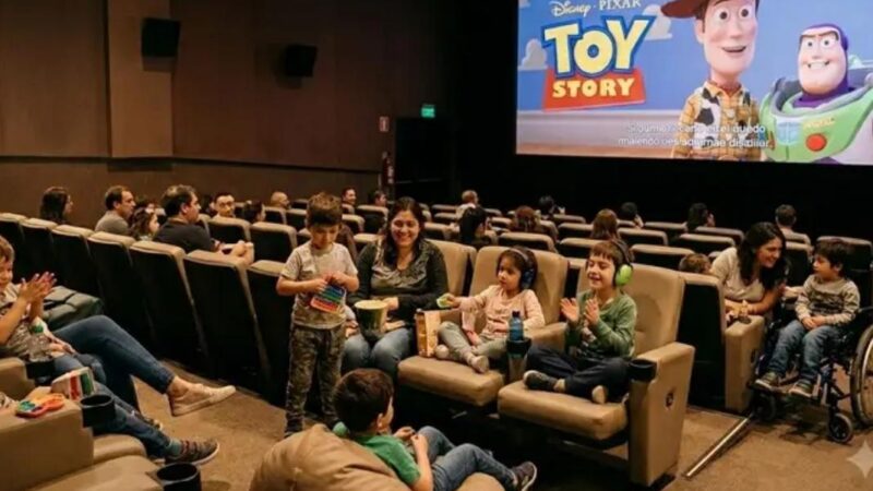 Diversas personas adultas e infantes en una sala de cine y en la pantalla imagen de la película Toy Story