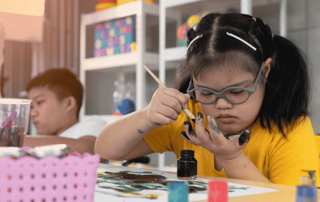 niña con síndrome de Down pintando y atrás otro niño