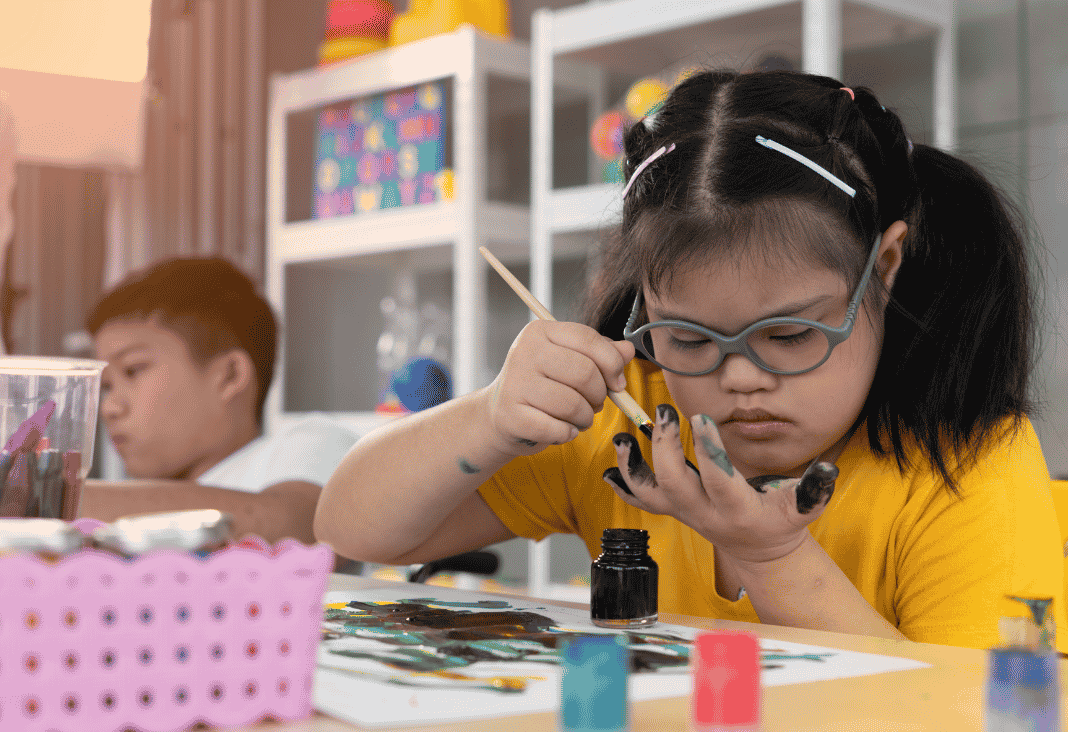 niña con síndrome de Down pintando y atrás otro niño
