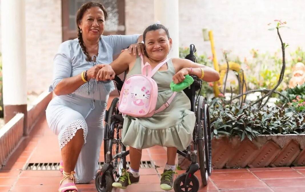 Mujer cuidadora junto a otra en silla de ruedas