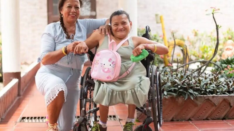 Mujer cuidadora junto a otra en silla de ruedas