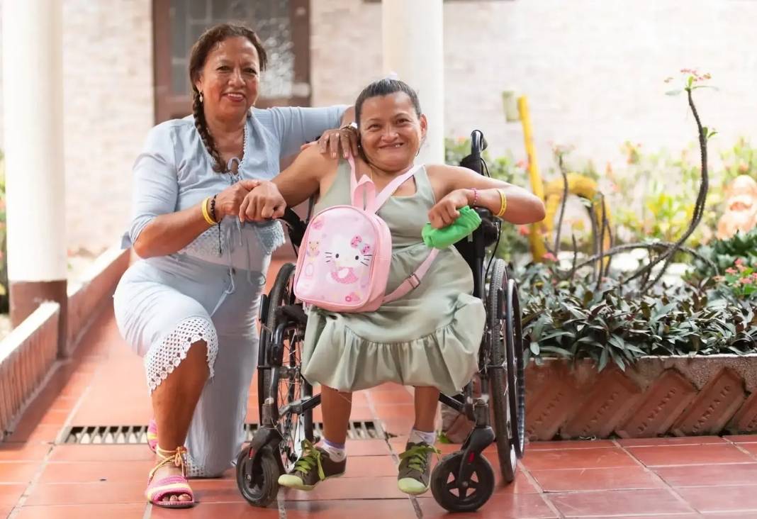 Mujer cuidadora junto a otra en silla de ruedas