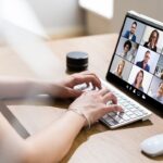 manos de mujer escribiendo teclado frente a una videollamada