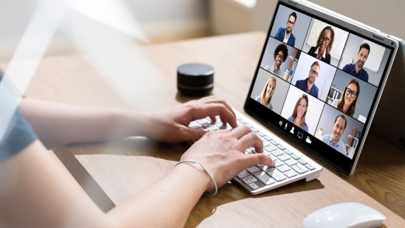 manos de mujer escribiendo teclado frente a una videollamada