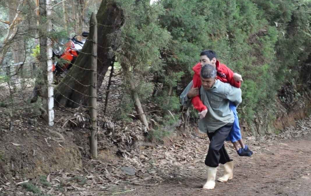 Hombre llevando en su espalda a un joven con discapacidad por un camino de piedra en el campo