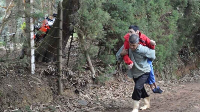 Hombre llevando en su espalda a un joven con discapacidad por un camino de piedra en el campo