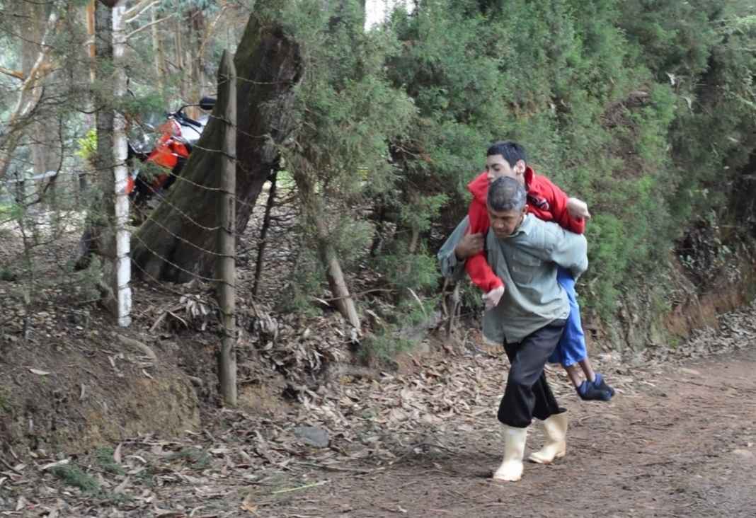 Hombre llevando en su espalda a un joven con discapacidad por un camino de piedra en el campo