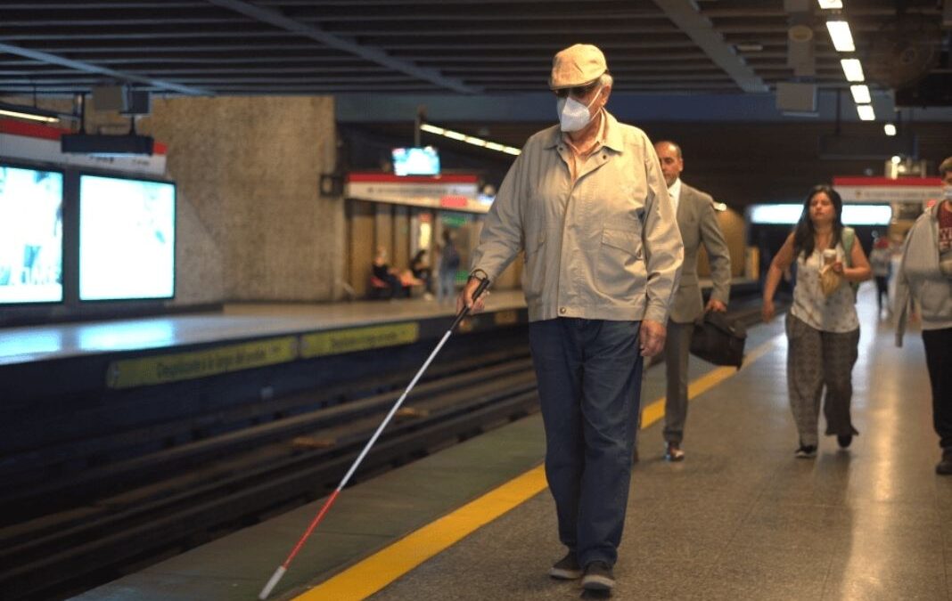 Un hombre ciego con su bastón caminando por anden de metro