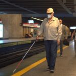 Un hombre ciego con su bastón caminando por anden de metro