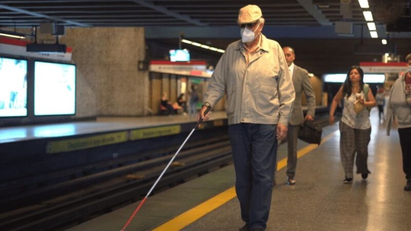 Un hombre ciego con su bastón caminando por anden de metro