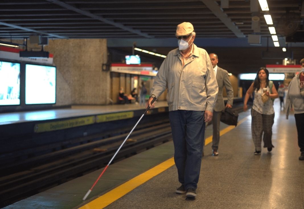Un hombre ciego con su bastón caminando por anden de metro