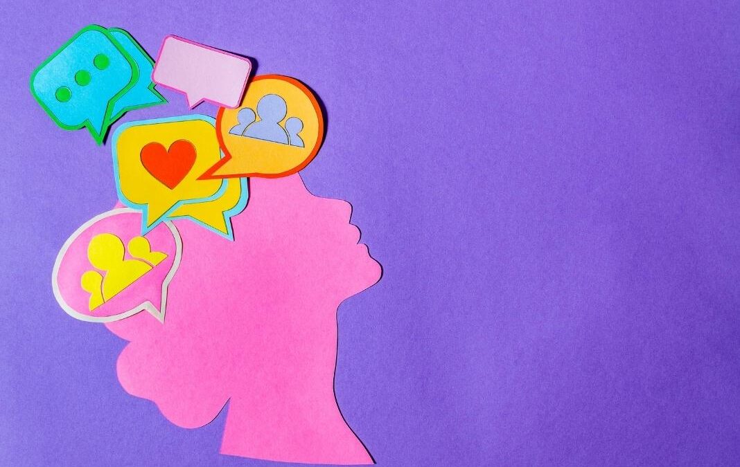 Silueta hecha con papel de una mujer con distintos emojis en su cerebro