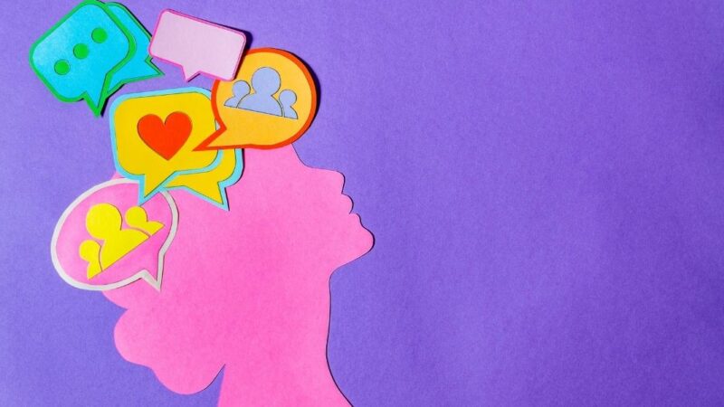 Silueta hecha con papel de una mujer con distintos emojis en su cerebro