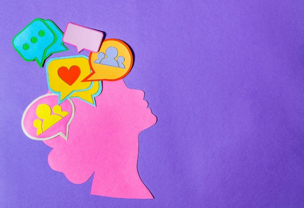 Silueta hecha con papel de una mujer con distintos emojis en su cerebro